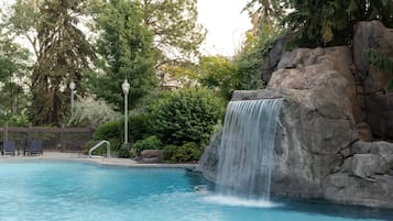 Une piscine agrémentée d’une cascade, entourée d’arbres et d’une clôture en bois.