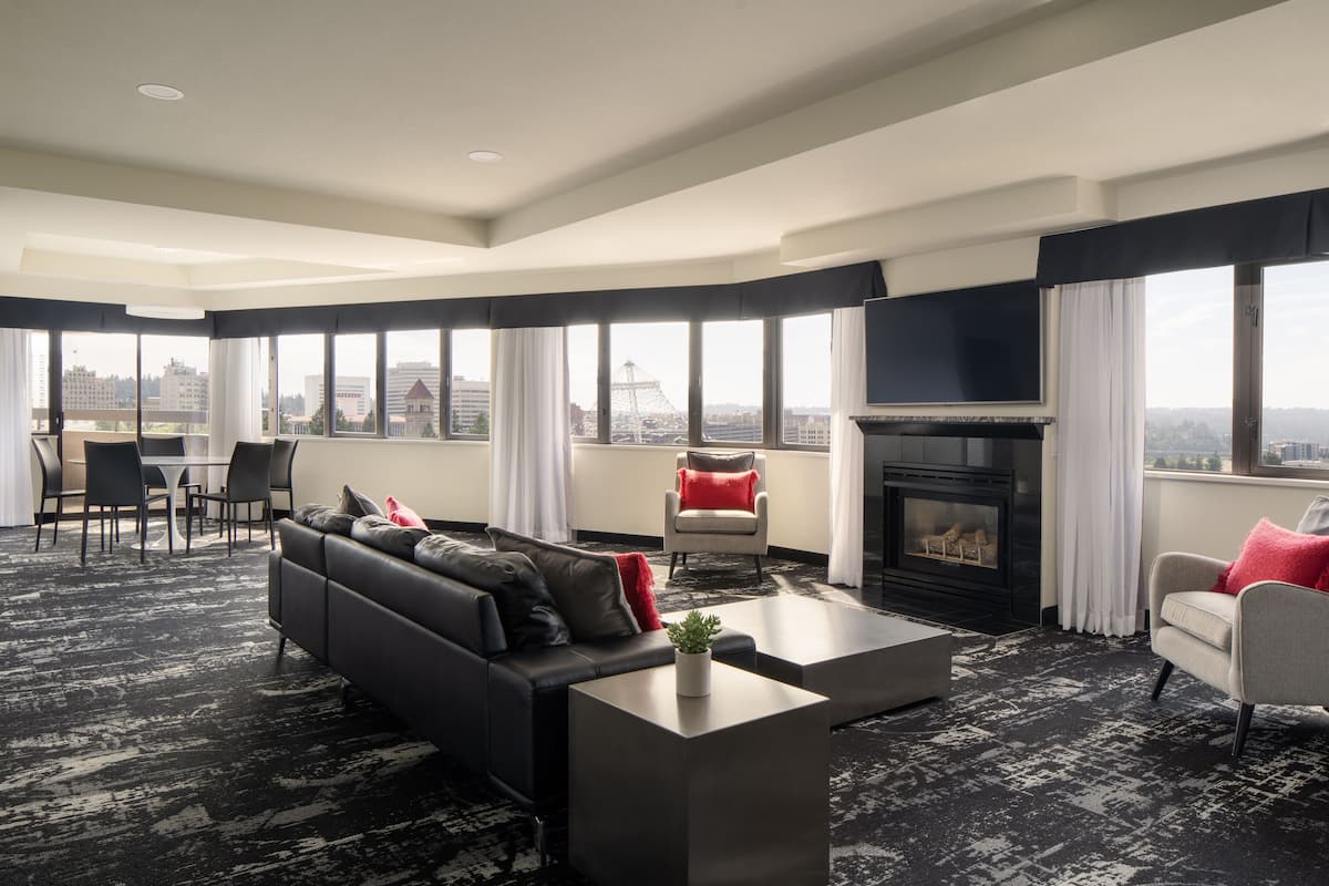 A modern living room with a black and white patterned carpet, a black sofa with red and grey cushions, a white armchair with a red cushion, a grey armchair with a red cushion, and a fireplace.