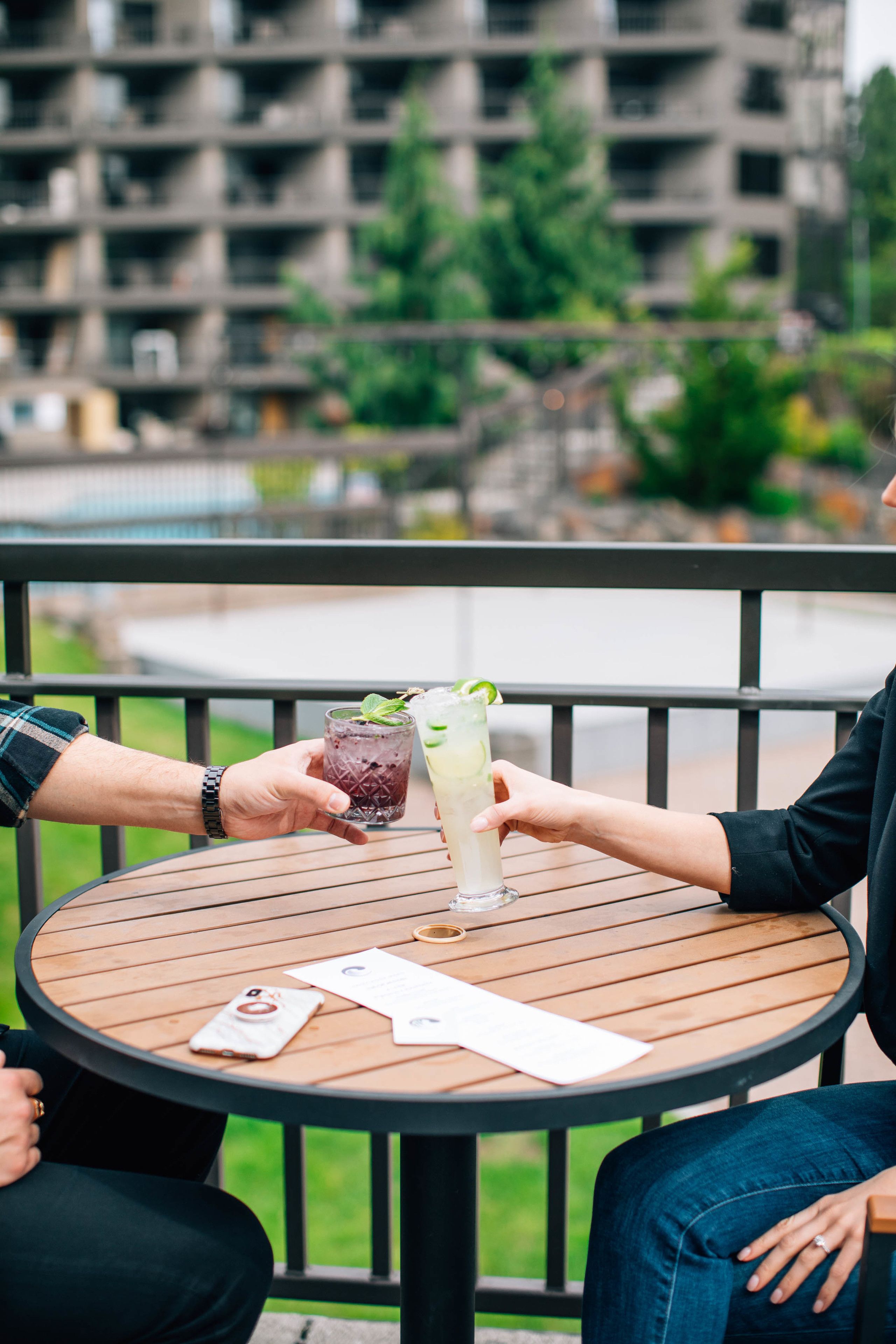 A round wooden table with two drinks, a menu, and a smartphone on it.