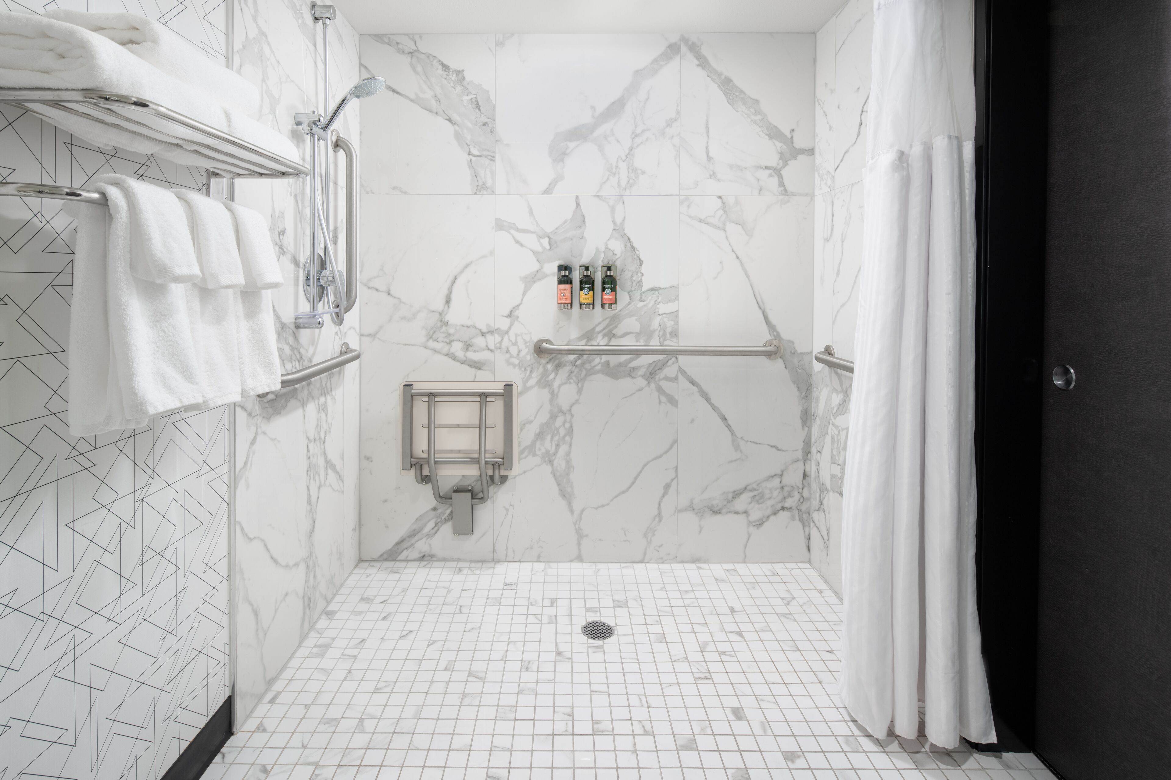 A modern bathroom with a shower area, marble walls, a towel rack, and a hand sanitizer dispenser.