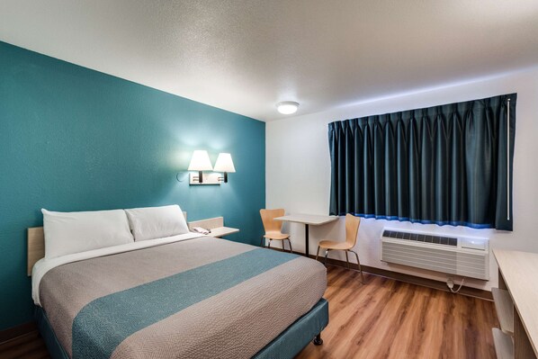 Habitación de hotel con cama, escritorio, dos sillas, ventana con cortinas y equipo de aire acondicionado.