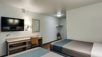 A hotel room with a bed, a desk with a chair, a TV, a mirror, and a hanging clothes rack.