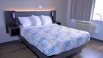 A modern hotel room with a large bed, a bedside table, a wall-mounted light, and a window with curtains.