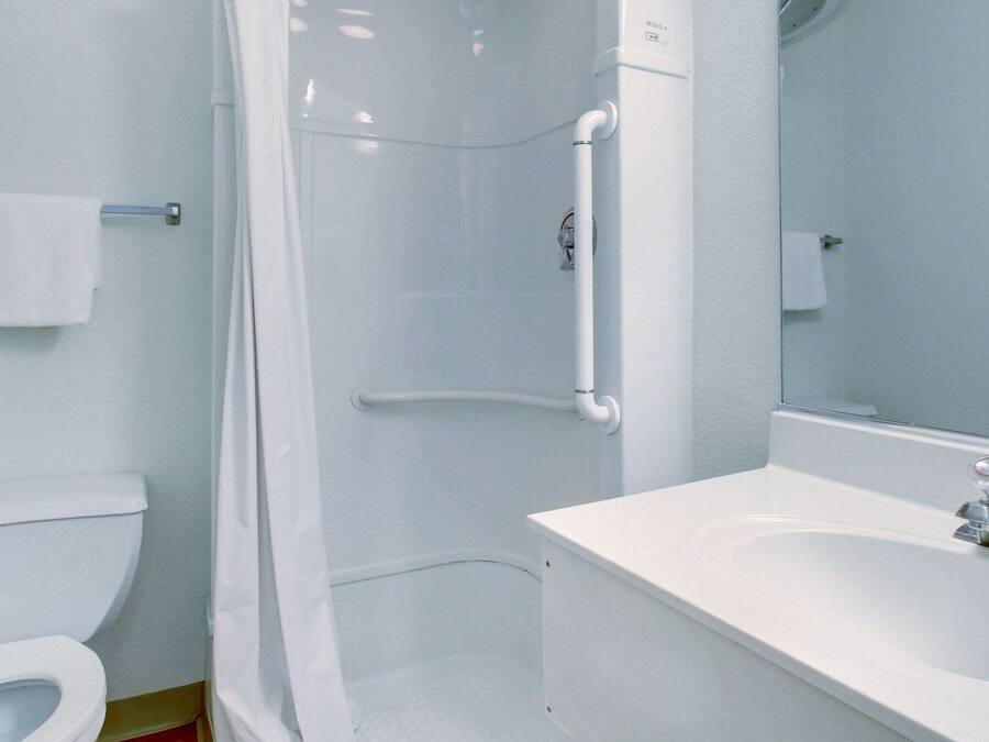 A bathroom with a toilet, a shower with a grab bar, and a sink with a mirror.