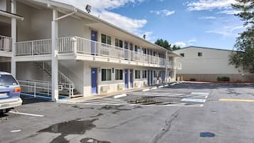 Een motel met een gebouw van twee verdiepingen, meerdere kamers en een parkeerplaats met kuilen.