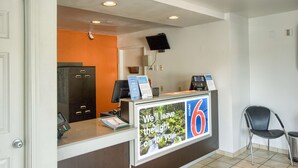 A hotel reception area with a counter, a television mounted on the wall, and a chair to the right.