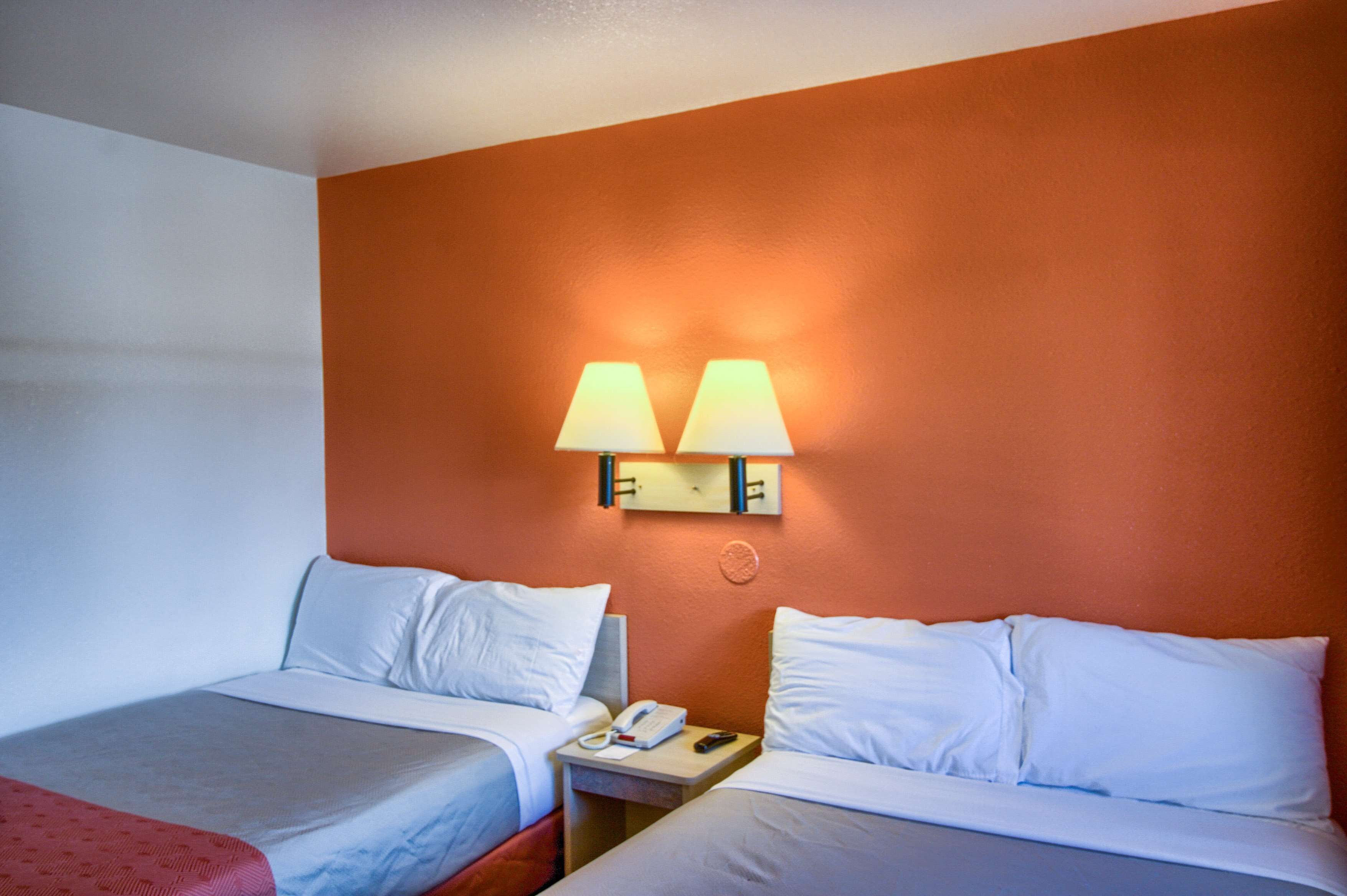 Ein Hotelzimmer mit zwei Betten, weißer Bettwäsche, einem Nachttisch mit Telefon und Lampe sowie einer orangefarbenen Wand.