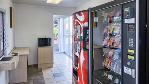 A vending machine with snacks and a microwave in a room with a sink and a small cabinet.
