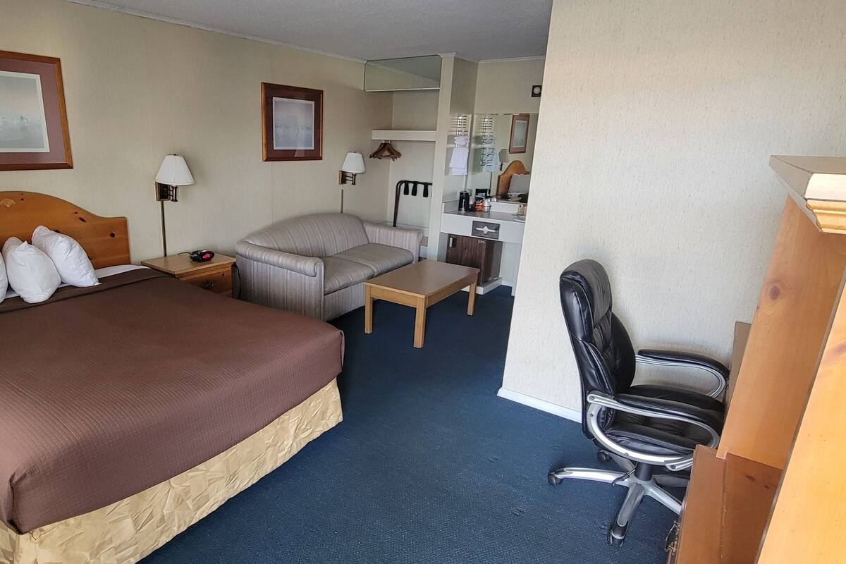 A hotel room with a large bed, a desk, a chair, and a wardrobe.