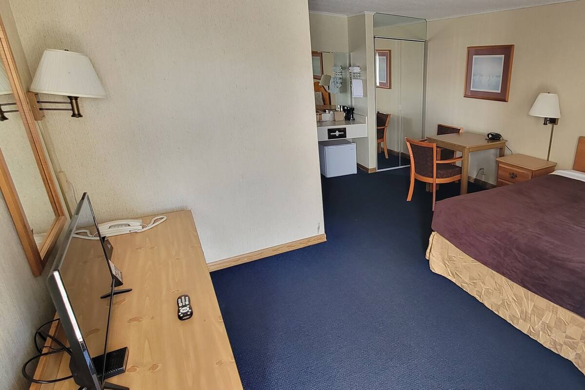 A hotel room with a large bed, a desk, a chair, a mirror, a lamp, and a television.