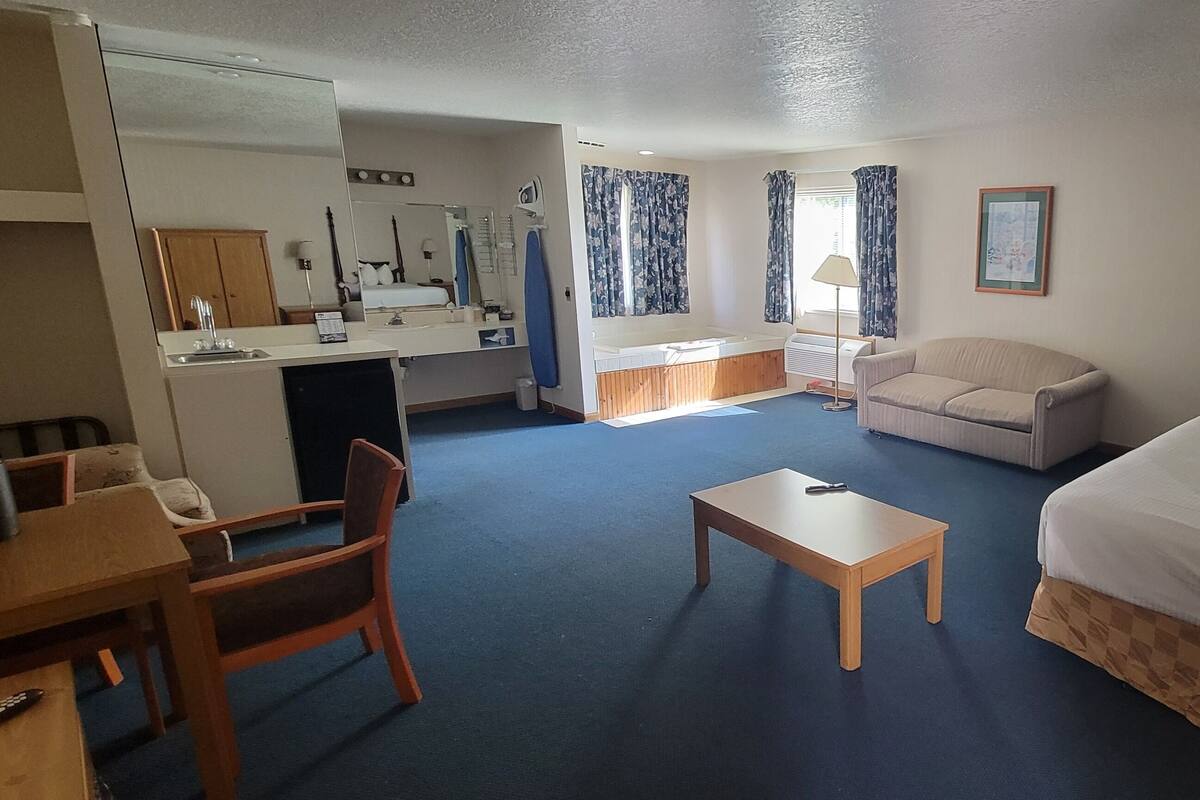 A hotel room with a bed, a desk with a chair, a small table, a sofa, and a large mirror.