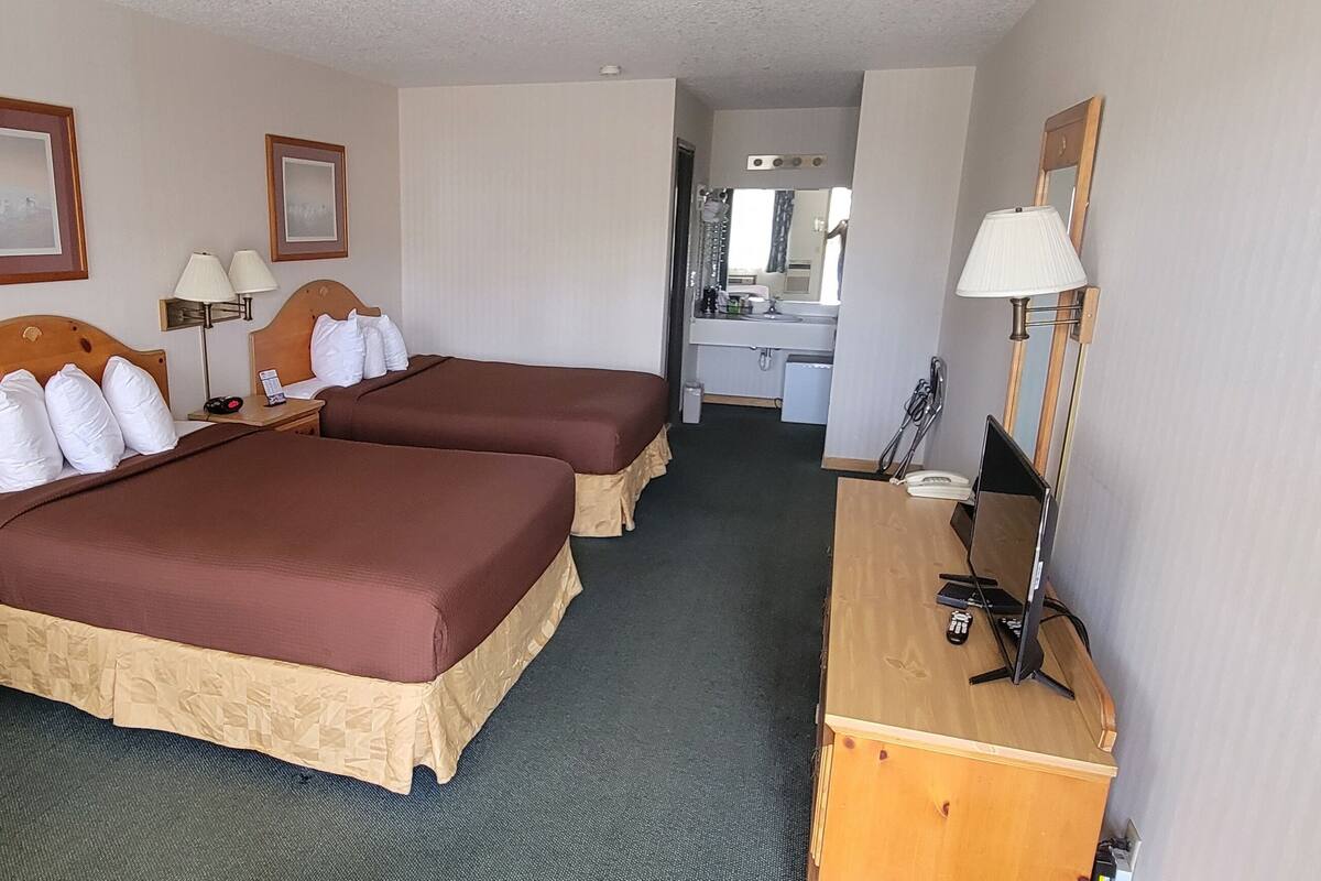A hotel room with two beds, a desk, a chair, a lamp, and a mirror.