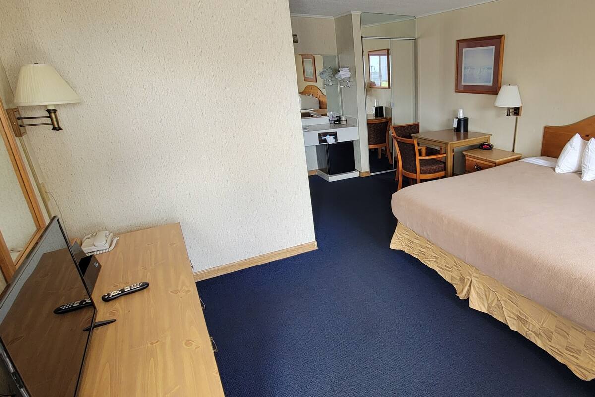 A hotel room with a large bed, a desk, a chair, a desk lamp, a telephone, and a laptop.