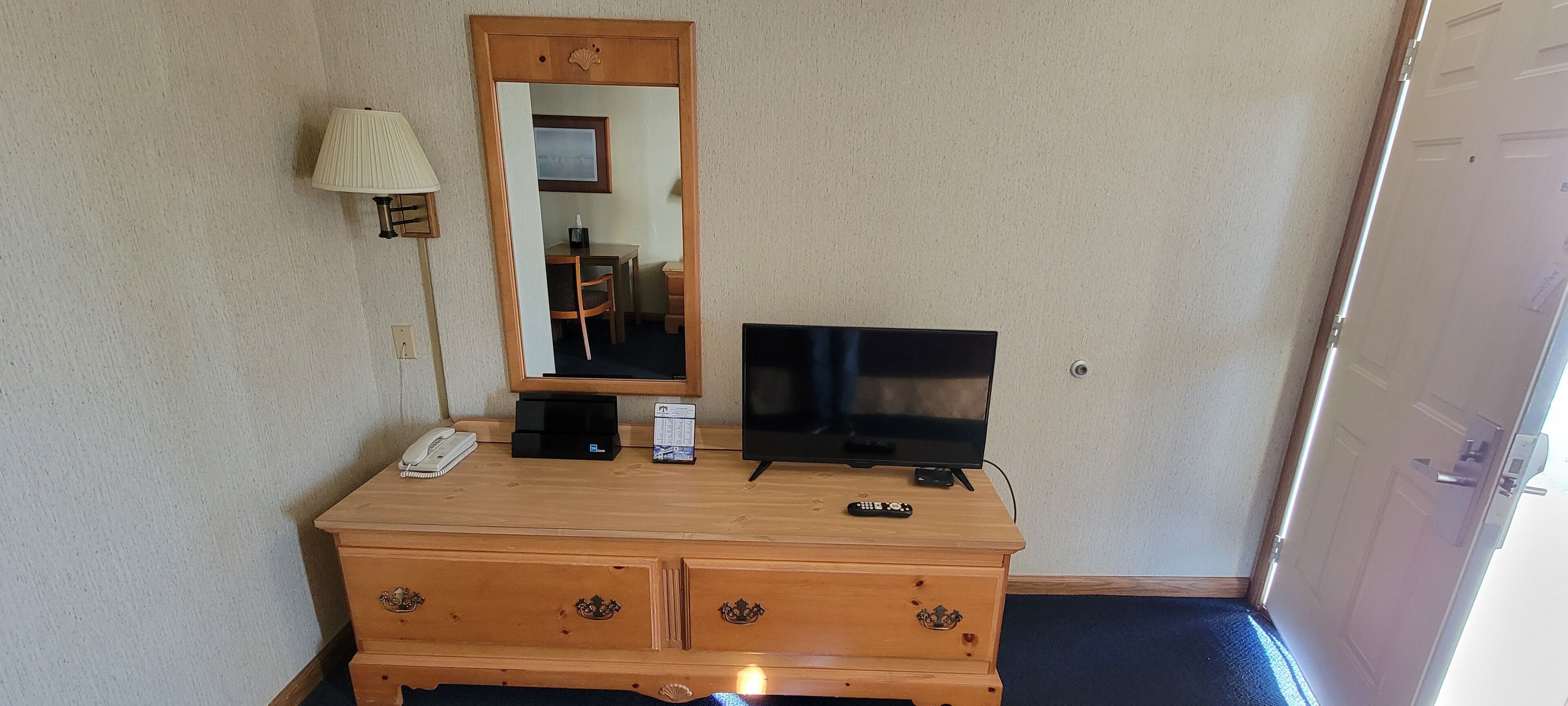 A wooden dresser with a flat-screen TV, a lamp, and a telephone.