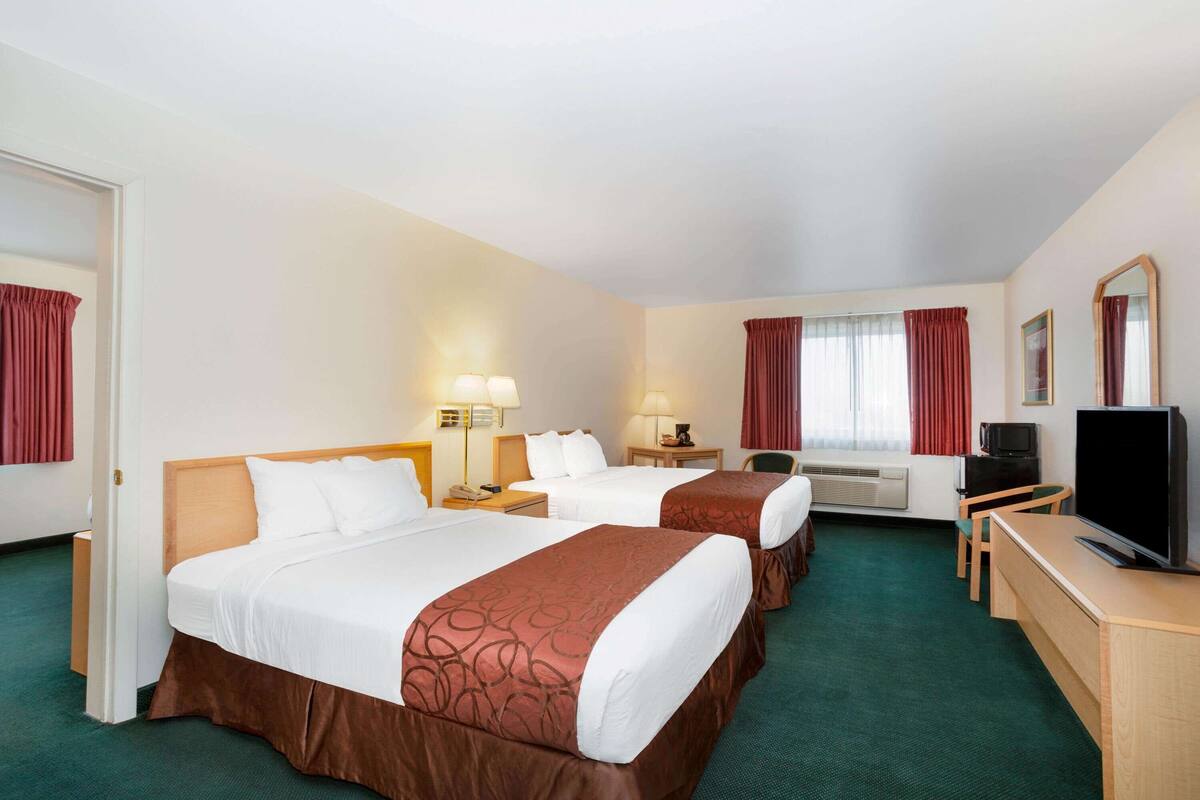 A hotel room with two beds, a desk, a television, and a mirror.