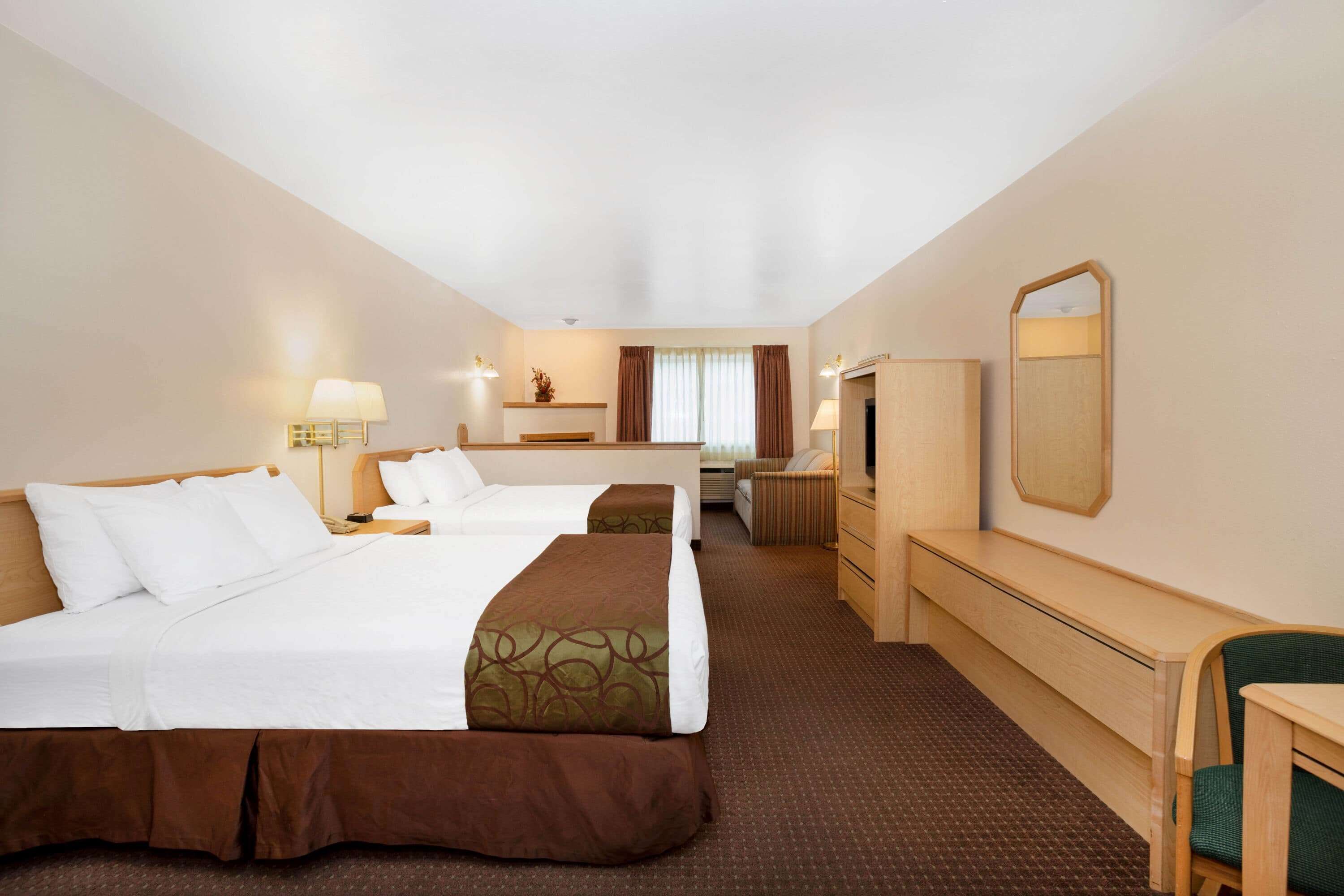 A hotel room with two beds, a desk, a chair, a dresser, and a mirror.