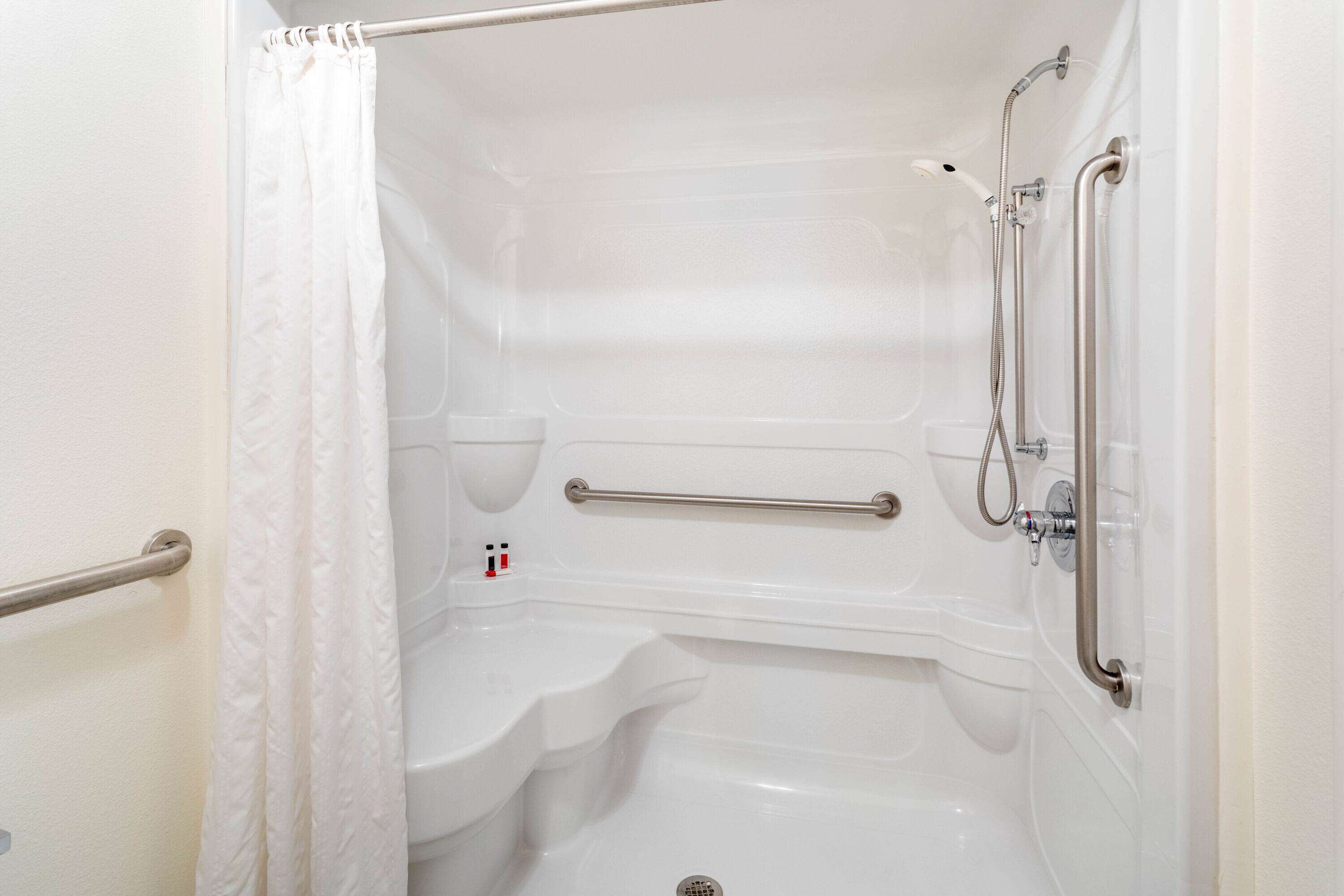 A white, accessible bathroom with a shower, grab bars, and a toilet.