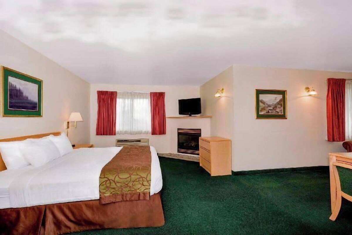 A hotel room with a bed, a television, a fireplace, and a desk.