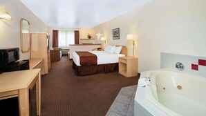 A hotel room with a bed, a desk, a TV, a bathroom with a bathtub, and a mirror. - Inn at Lander, Travelodge by Wyndham (Lander)