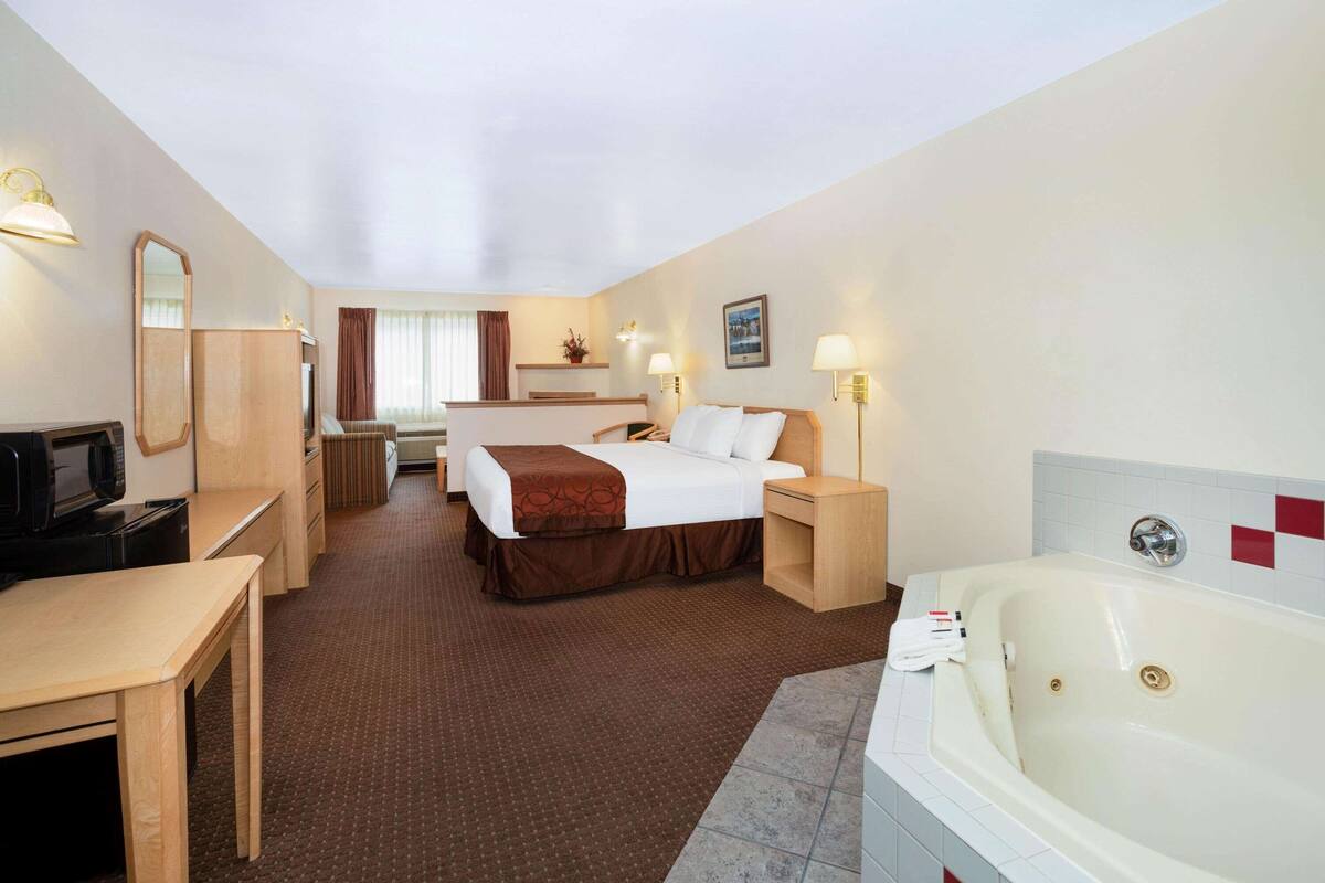 A hotel room with a bed, a desk, a TV, a bathroom with a bathtub, and a mirror.
