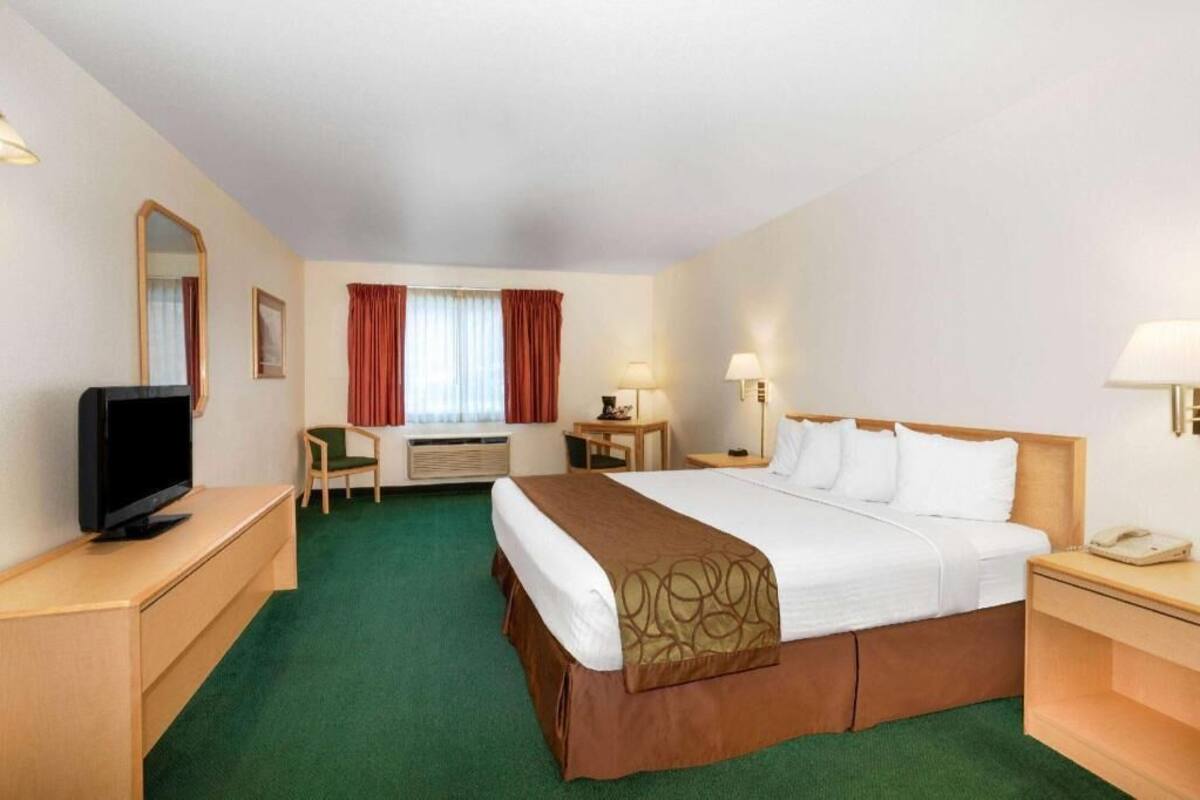 A hotel room with a bed, a desk, a television, a chair, a lamp, and a window with curtains.