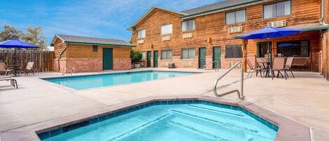 A pool area with a wooden building, outdoor seating, and a clear blue sky.