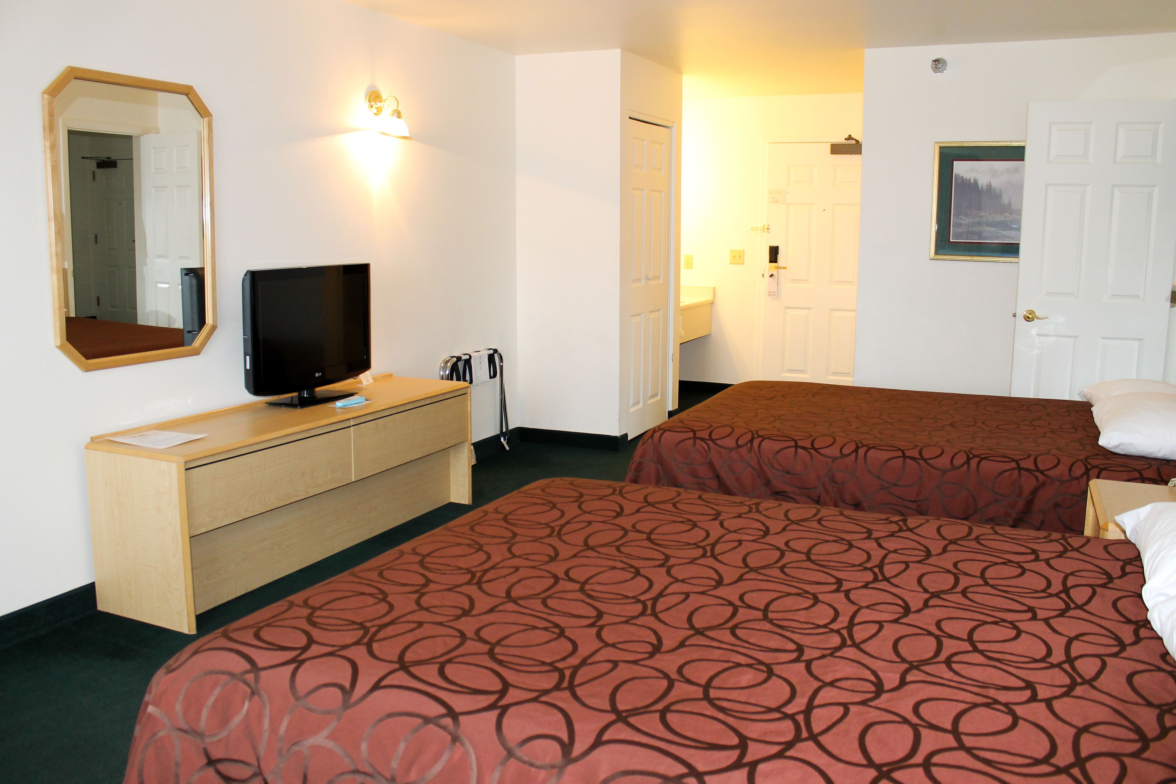 A hotel room with two beds, a TV on a wooden dresser, a mirror, and a door with a picture frame.