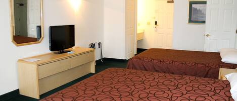 A hotel room with two beds, a TV on a wooden dresser, a mirror, and a door with a picture frame.