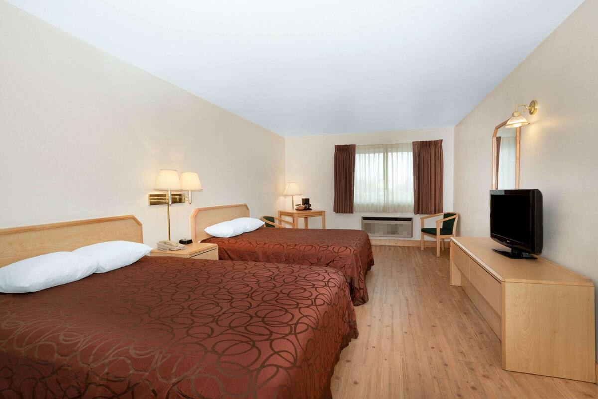 A hotel room with two beds, a desk, a television, and a window with curtains.