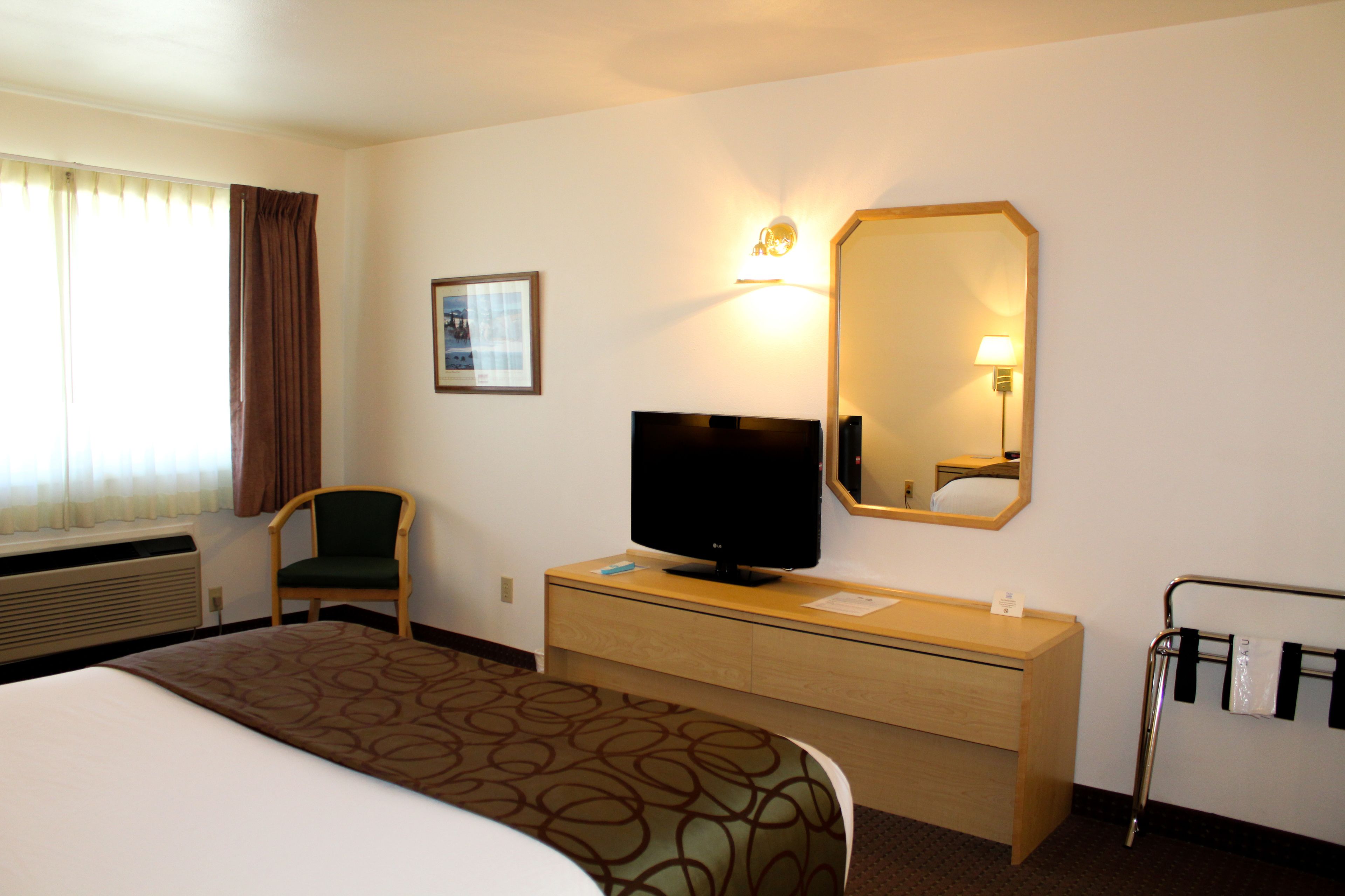 A hotel room with a bed, a television, a desk, a chair, a mirror, and a window with curtains.