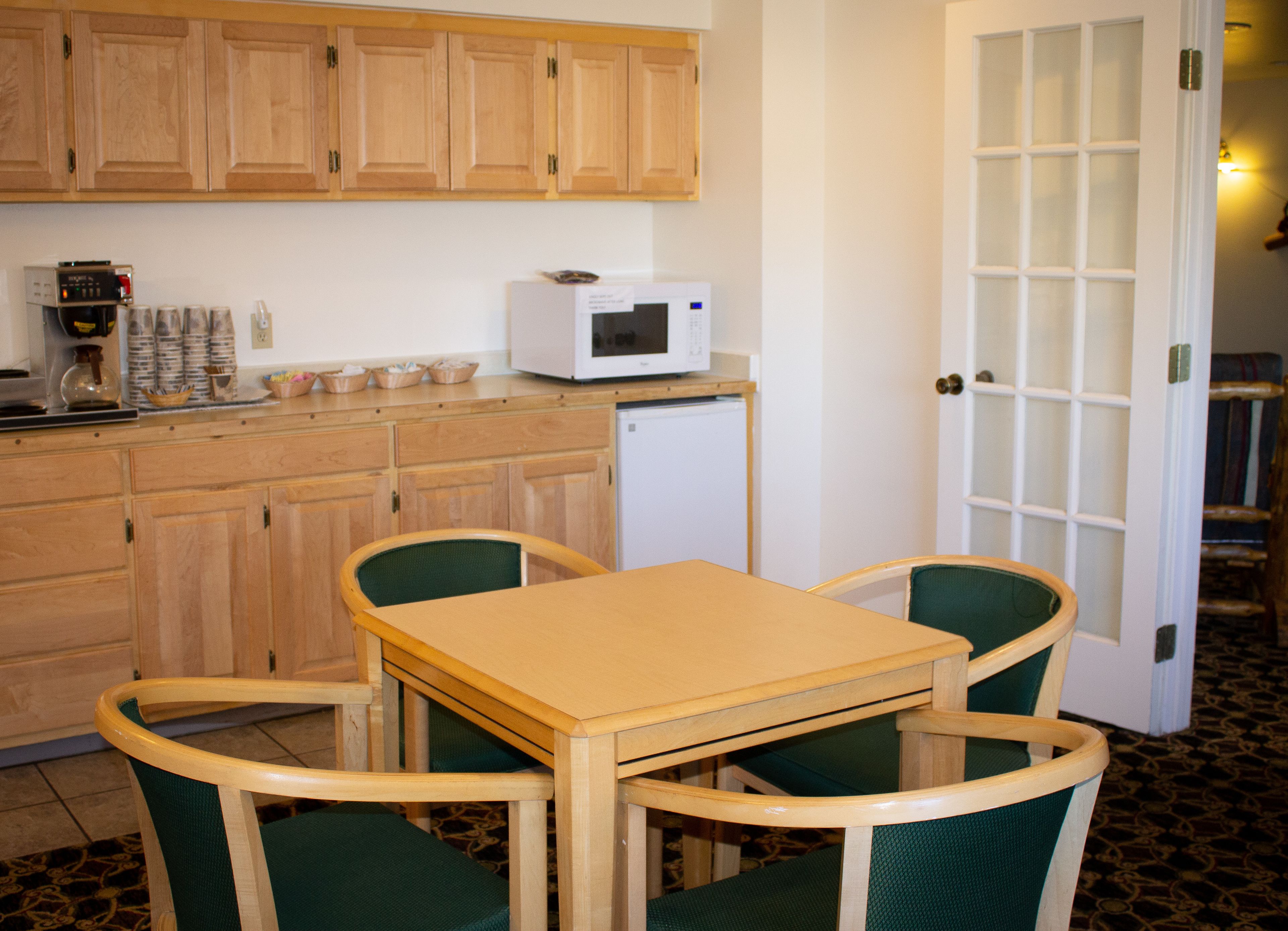 A small kitchen with wooden cabinets, a microwave, and a coffee maker. There is a table with two chairs.