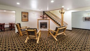 A room with a patterned carpet, wooden chairs, a small table, a fireplace, and a staircase. - Inn at Lander, Travelodge by Wyndham (Lander)