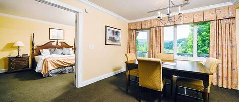 A hotel room with a bed, a dining table with chairs, a chandelier, and a window with curtains.