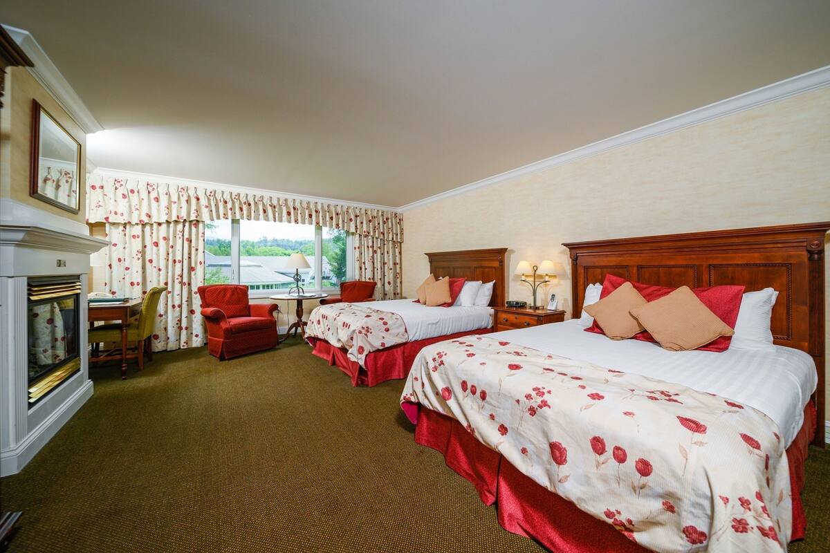 A hotel room with two beds, a fireplace, a desk, and a window with curtains.