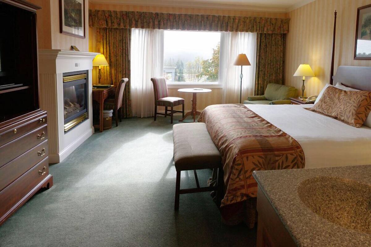 A hotel room with a bed, a desk with a lamp, a chair, a small table, and a view of the outdoors.
