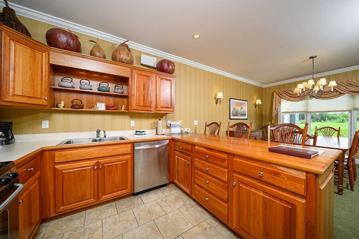 A kitchen with wooden cabinets, a stainless steel dishwasher, and a dining area with a large wooden table and chairs.