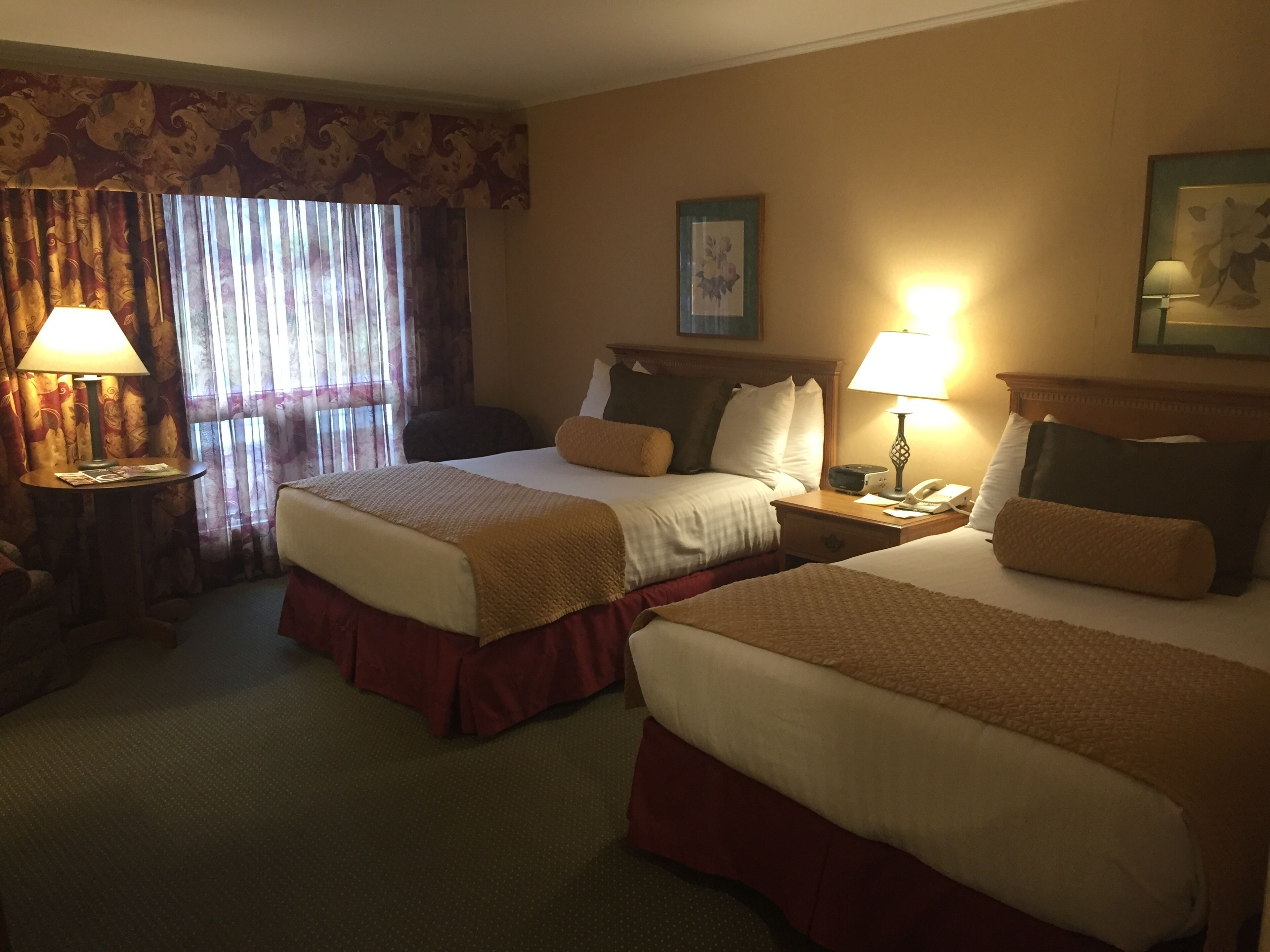A hotel room with two beds, a desk, a chair, a lamp, and a window with curtains.