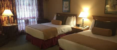 A hotel room with two beds, a desk, a chair, a lamp, and a window with curtains.