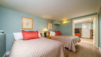 Une chambre d’hôtel avec deux lits, une table de chevet avec une lampe et une porte donnant sur une autre pièce.
