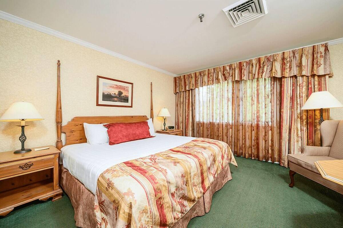 A hotel room with a large bed, two bedside tables with lamps, a chair, a painting on the wall, and a window with curtains.