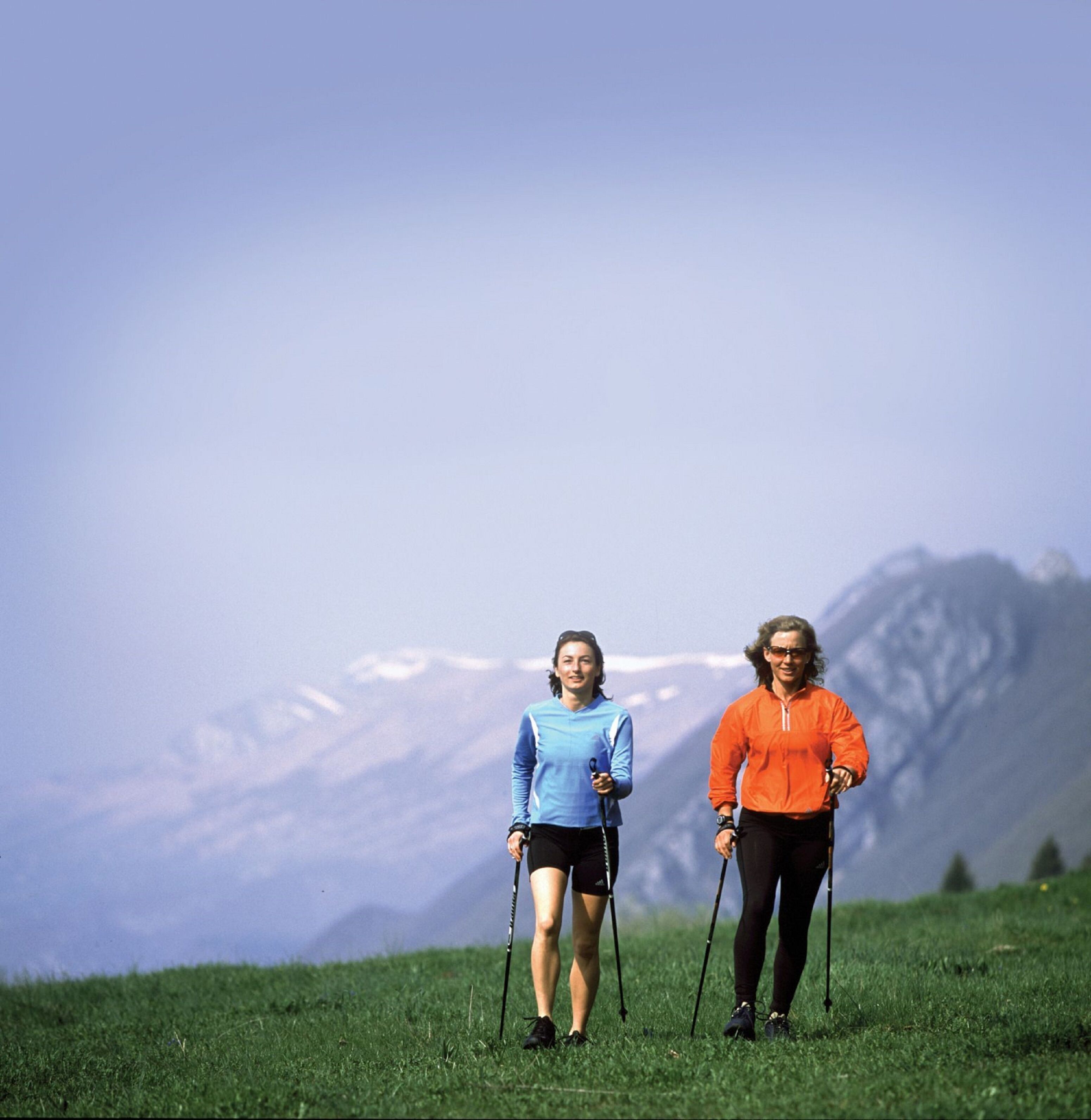 Two people hiking in a grassy field with a mountain in the background.
