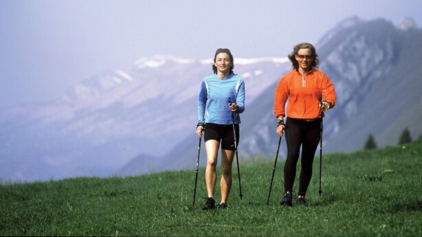 Two people hiking in a grassy field with a mountain in the background. - Stoweflake Mountain Resort & Spa (Stowe)