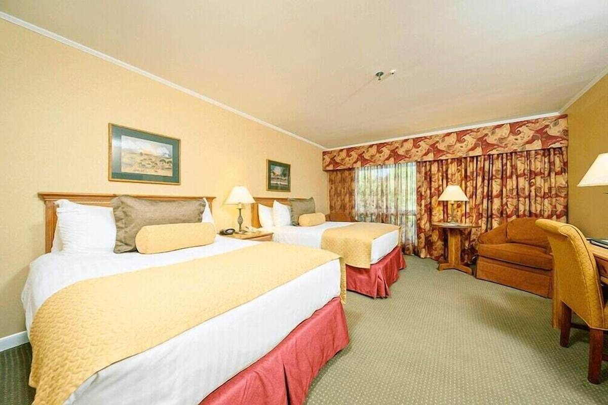 A hotel room with two beds, a desk, a chair, and a window with curtains.