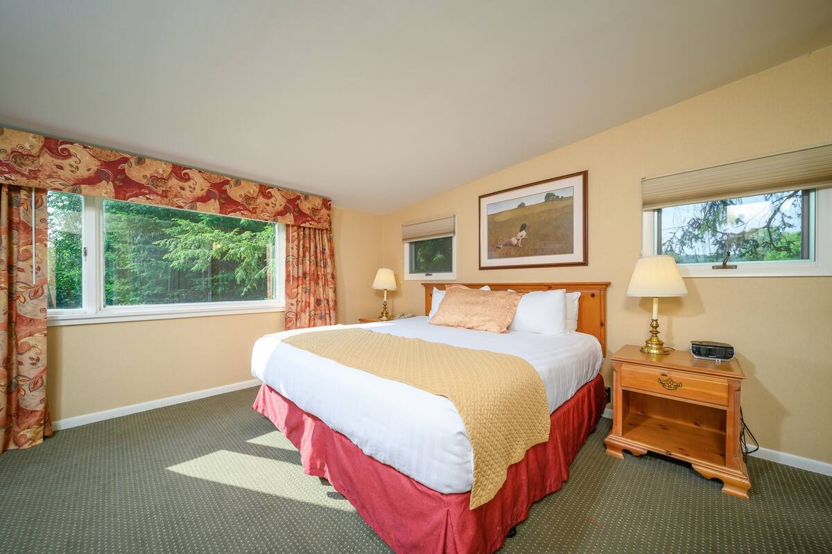A hotel room with a large bed, two bedside lamps, a nightstand, and a window with curtains.