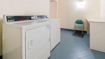 Zona de lavandería con dos secadoras y una silla.