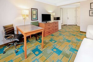 Ein Hotelzimmer mit einem Holztisch, einem Fernseher, einer Mikrowelle, einem Sessel und einem gemusterten Teppich.