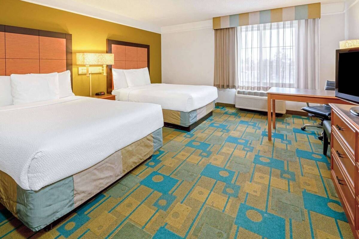 Quarto de hotel com duas camas, uma escrivaninha, uma televisão e uma janela com cortinas.