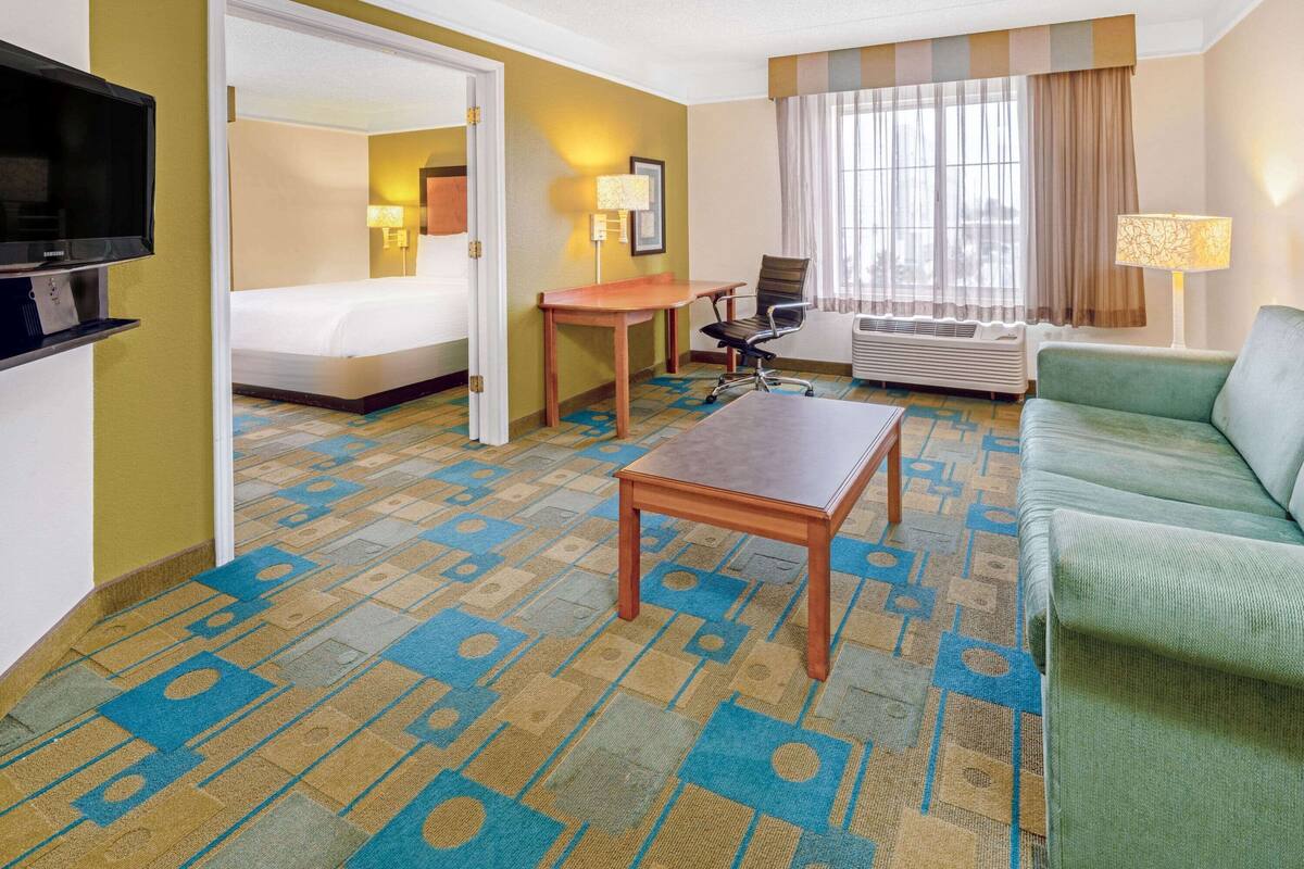 Quarto de hotel com uma cama, uma escrivaninha, um sofá verde e uma televisão.