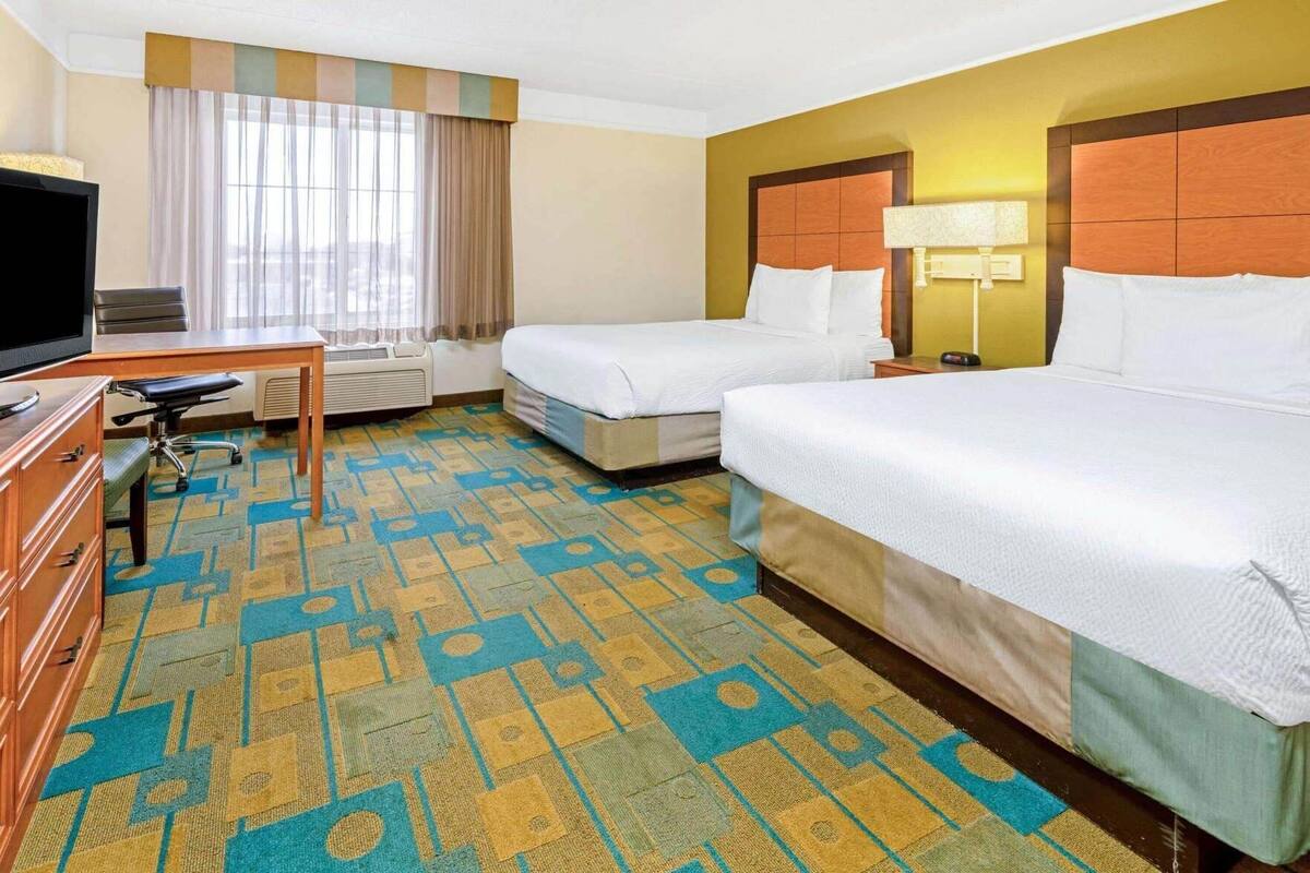 Quarto de hotel com duas camas, uma mesa, uma televisão e uma janela com cortinas.