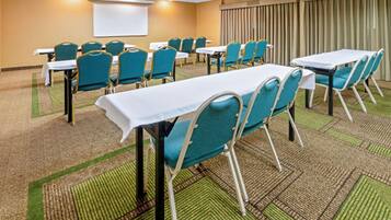 A conference room with tables and chairs, carpeted floor, and a projector screen on the wall.